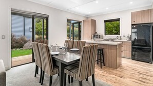 A modern kitchen with a central island, wooden cabinetry, and a built-in refrigerator. - Cardrona Cottage - Cardrona Holiday Home (Cardrona)