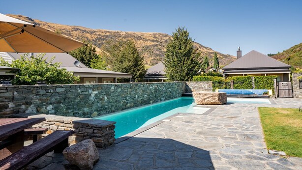 A backyard with a swimming pool, stone patio, picnic tables, and a stone wall. - Cardrona Cottage - Cardrona Holiday Home (Cardrona)