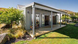 A modern house with a covered patio, a lawn, and a hillside in the background. - Cardrona Cottage - Cardrona Holiday Home (Cardrona)