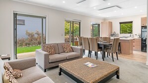 A modern living room with a sofa, coffee table, and dining area with striped chairs. - Cardrona Cottage - Cardrona Holiday Home (Cardrona)