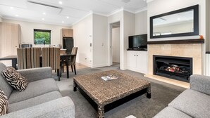 A modern living room with a fireplace, grey sofas, a coffee table, and a TV. - Cardrona Cottage - Cardrona Holiday Home (Cardrona)