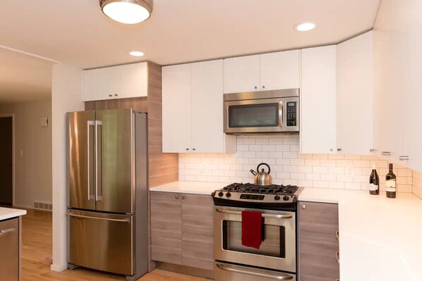 A modern kitchen with stainless steel appliances, white cabinetry, and a tiled backsplash.