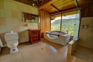 Un bany amb vàter, lavabo, banyera i una finestra gran que ofereix vistes a un paisatge de muntanya.