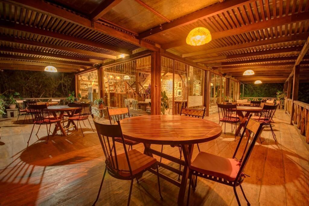 An indoor dining area with wooden tables and chairs, large windows, and a stone wall.