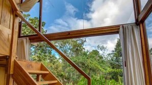 Una escalera de madera que lleva a un balcón con vistas a abundante vegetación.