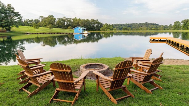 A lakeside setting with a fire pit and Adirondack chairs.