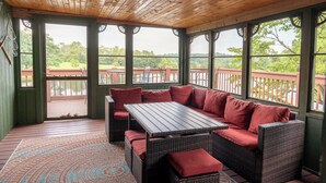 A covered patio with wicker furniture and a view of a wooden deck and greenery.