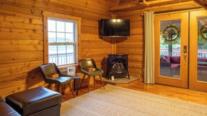 A log cabin interior with a fireplace, two chairs, a sofa, a TV, and a door with a wreath.