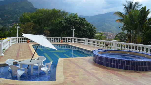 A swimming pool with a view of mountains, a hot tub, and a covered seating area with a table and chairs. - Hotel campestre (Copacabana)