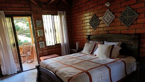 A bedroom with a brick wall, a bed with a quilt, a wooden rocking chair, and a small table with a lamp. - Hotel campestre (Copacabana)