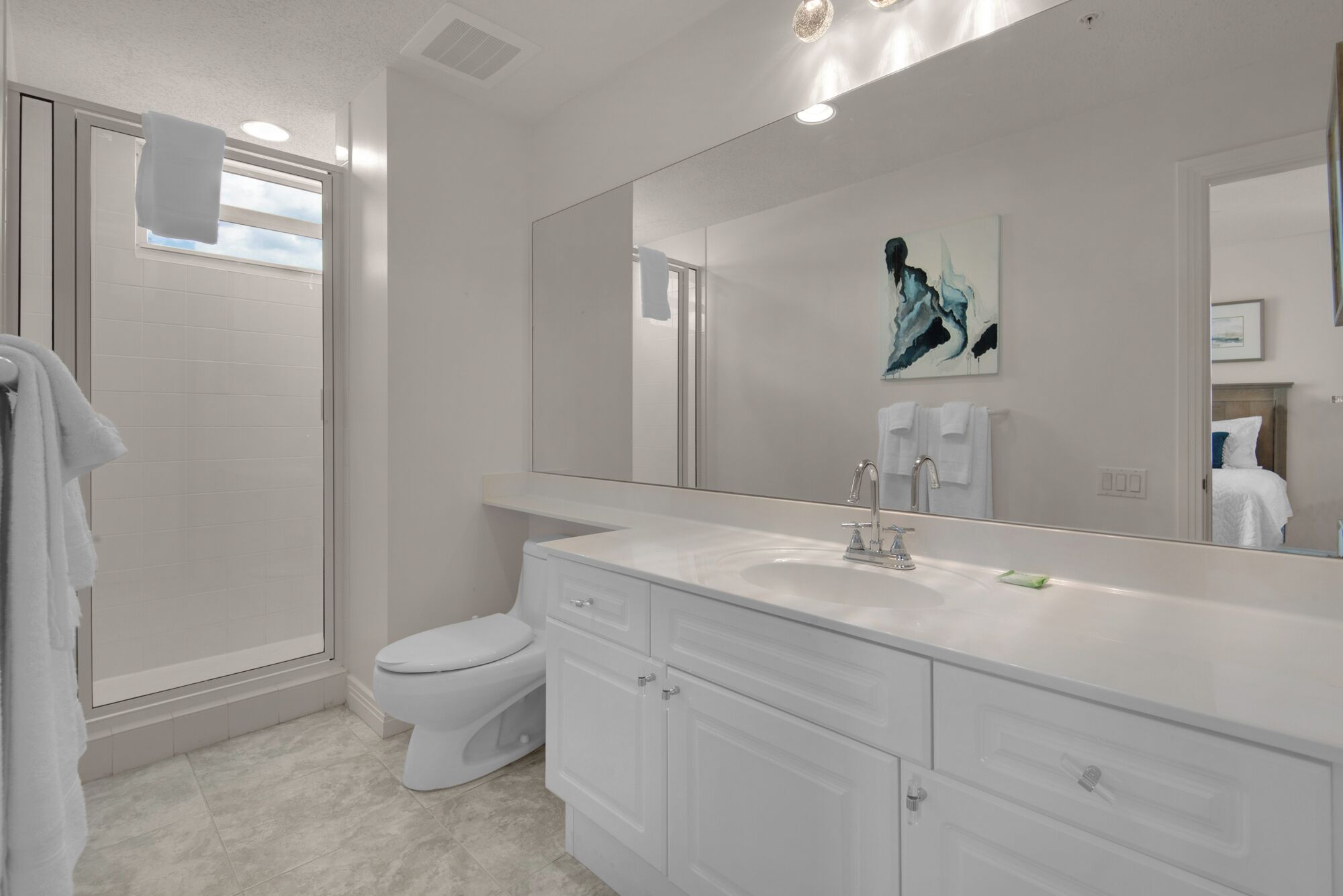 A modern bathroom with a large mirror, white fixtures, and a toilet.