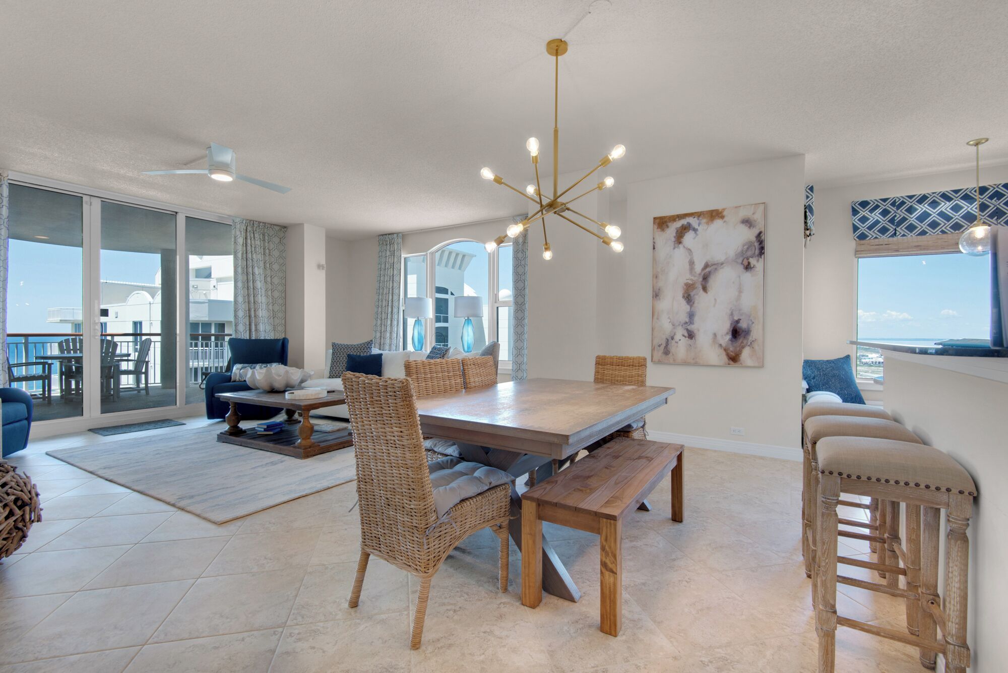 A spacious living room with a large wooden dining table, wicker chairs, and a modern chandelier.