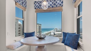 Un coin salon avec des sièges disposés en cercle autour d’une table ronde, des coussins à motifs bleus et une vue sur la plage et les bâtiments.