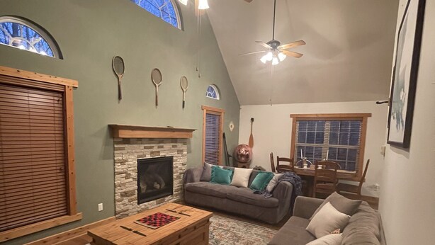 Un salon chaleureux avec une cheminée, un ventilateur de plafond et une grande fenêtre.