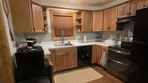 Une cuisine moderne avec des meubles en bois, un réfrigérateur noir, une cuisinière et un lave-vaisselle.
