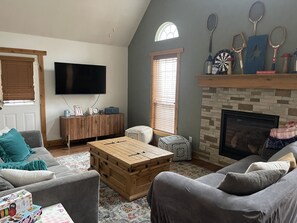 A living room with a flat-screen TV, a fireplace, and a collection of sports rackets. - Cozy, cabin in the woods perfect for hanging out. (Savannah)