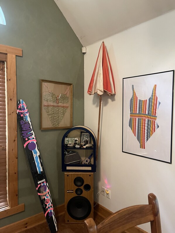 A room with a wooden floor, a framed picture on the wall, a speaker, and a colorful object leaning against the wall. - Cozy, cabin in the woods perfect for hanging out. (Savannah)
