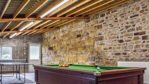 Une table de billard dans une pièce aux poutres apparentes et au mur en pierre.