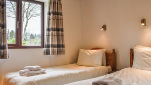 Une chambre avec deux lits simples, une fenêtre avec des rideaux et un luminaire fixé au mur.