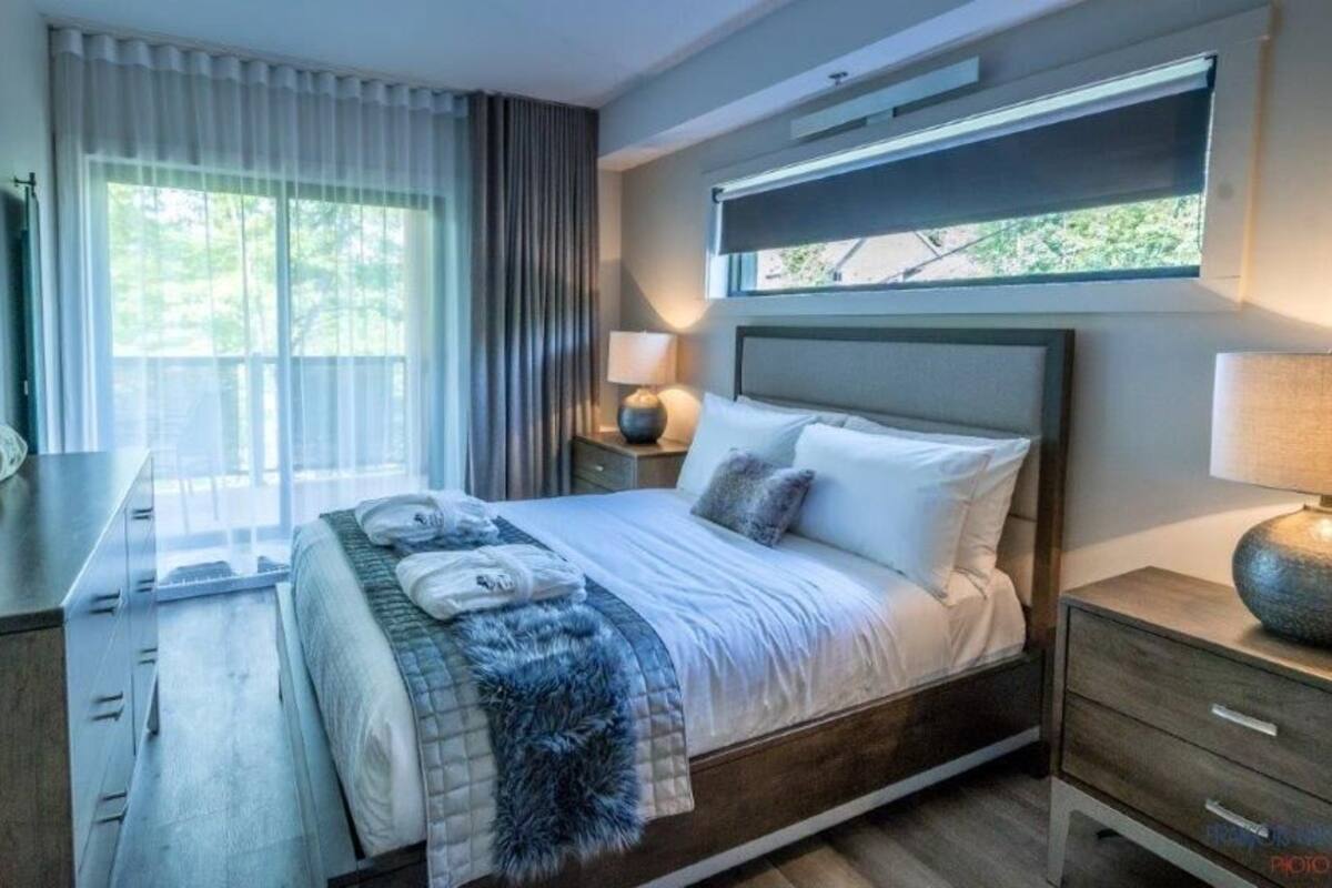 A modern hotel room with a large bed, a bedside table, a lamp, and a window with curtains.