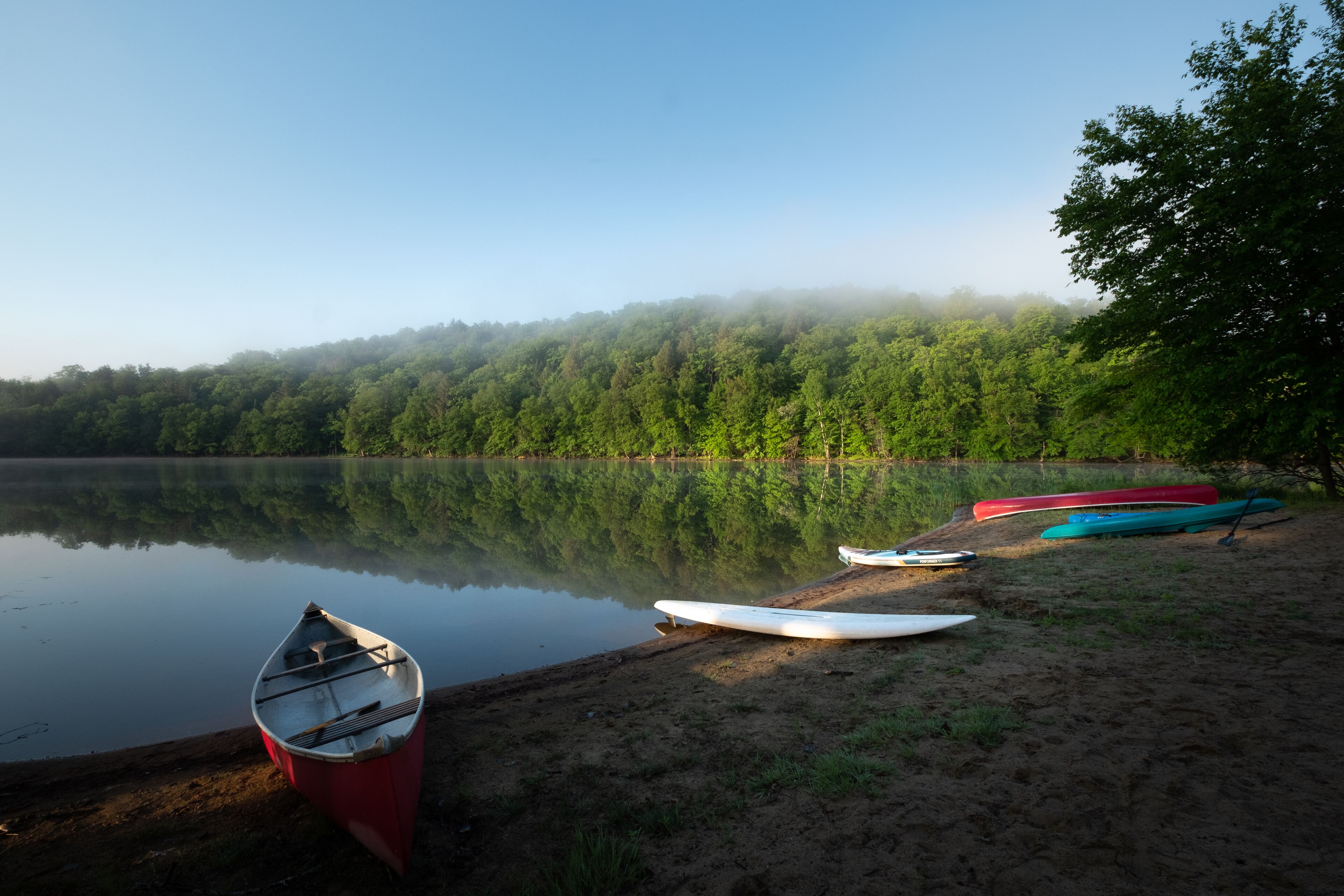 Un lago tranquilo con varias canoas y kayaks en la orilla.