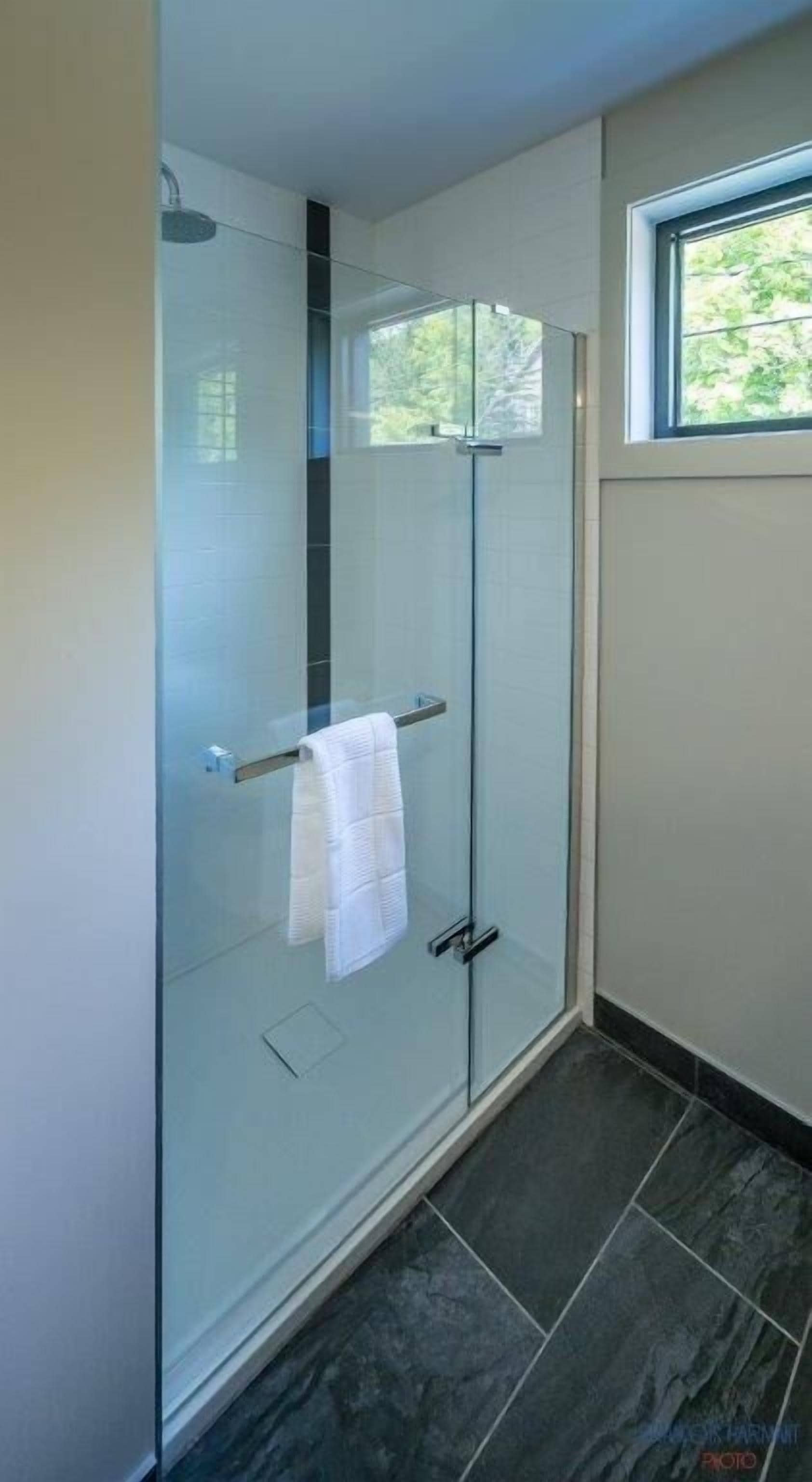 A modern bathroom with a glass shower enclosure, a towel rack, and a window providing natural light.