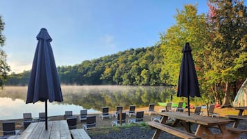 See-Szene mit Picknicktischen und -stühlen, umgeben von Bäumen und einem Zelt.