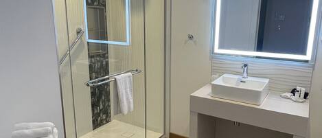 A modern bathroom with a glass shower enclosure, a vanity with a mirror, and a stack of towels.