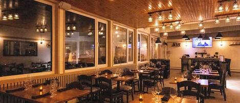 A restaurant with wooden tables and chairs, large windows, and hanging pendant lights.