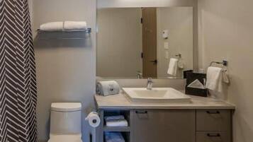 Un baño moderno con inodoro, lavabo y espejo. Hay toallas y artículos de aseo en la encimera.