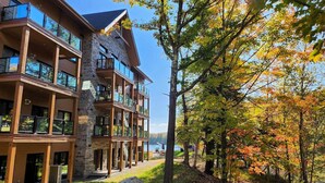 Un hotel de varios pisos con balcones, fachada de piedra y vista a un lago rodeado de árboles.