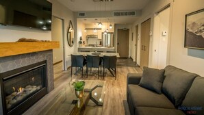 Una sala de estar moderna con chimenea, un sofá, un comedor con sillas y una cocina al fondo.