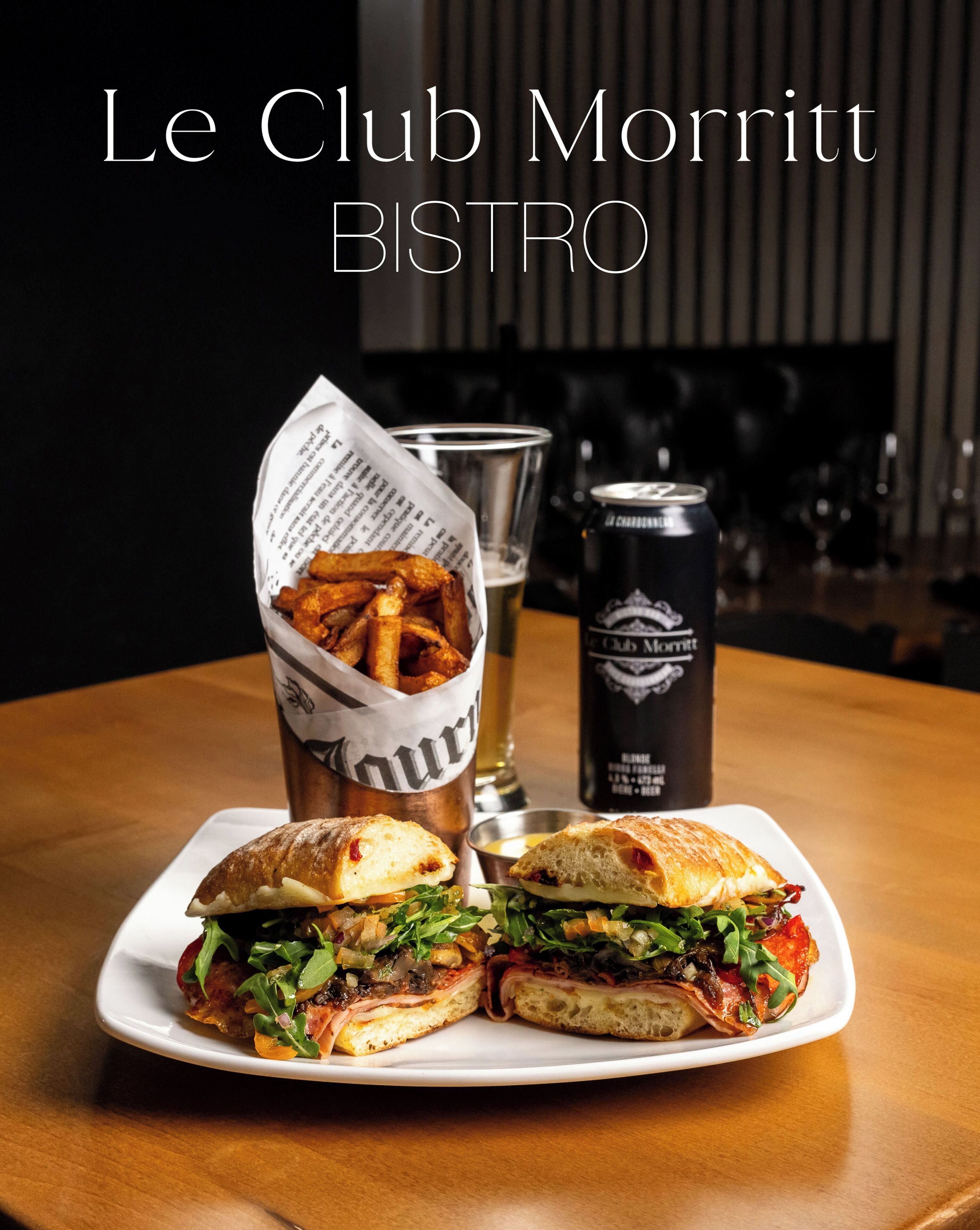 Ein Sandwich und Pommes auf einem Teller, dazu ein Getränk und eine Dose Bier.