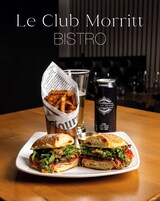 Un sándwich con papas fritas en un plato, acompañado de una bebida y una lata de cerveza.