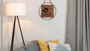 Una stanza con una lampada moderna, un cartello circolare fissato al muro con un motivo a foglia e la scritta STAY awhile, e un divano con cuscini decorati.