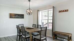 Zona pranzo con tavolo e sedie in legno, lampadario a sospensione, una panca e finestra con tende.
