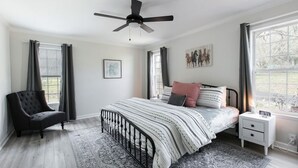 Una camera da letto con un letto, comodino, sedia e una ventola a soffitto.