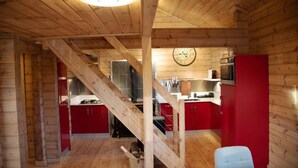 L’intérieur d’un chalet en bois comprend une cuisine, des placards rouges, un escalier et une horloge au mur.