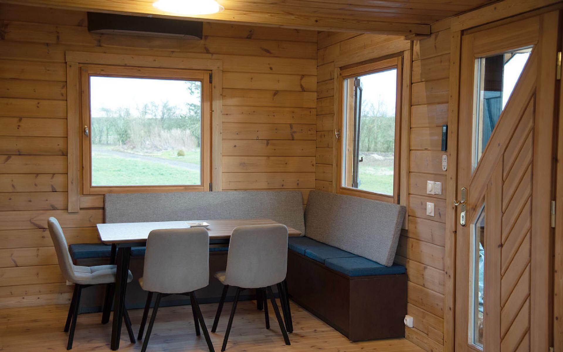 L’intérieur d’une cabane est aménagé avec du bois, il y a un banc, une table et deux chaises.