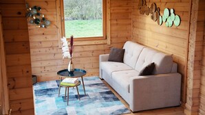 L’intérieur d’un chalet accueillant, avec un canapé, une petite table ornée d’un vase et une fenêtre donnant sur les arbres.