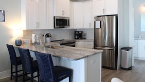 A kitchen with white cabinets, stainless steel appliances, a marble island, and bar stools.