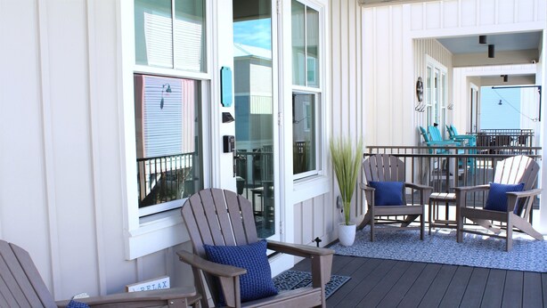A deck with wooden chairs and a table, a potted plant, and a sign that reads 'RELAX'.