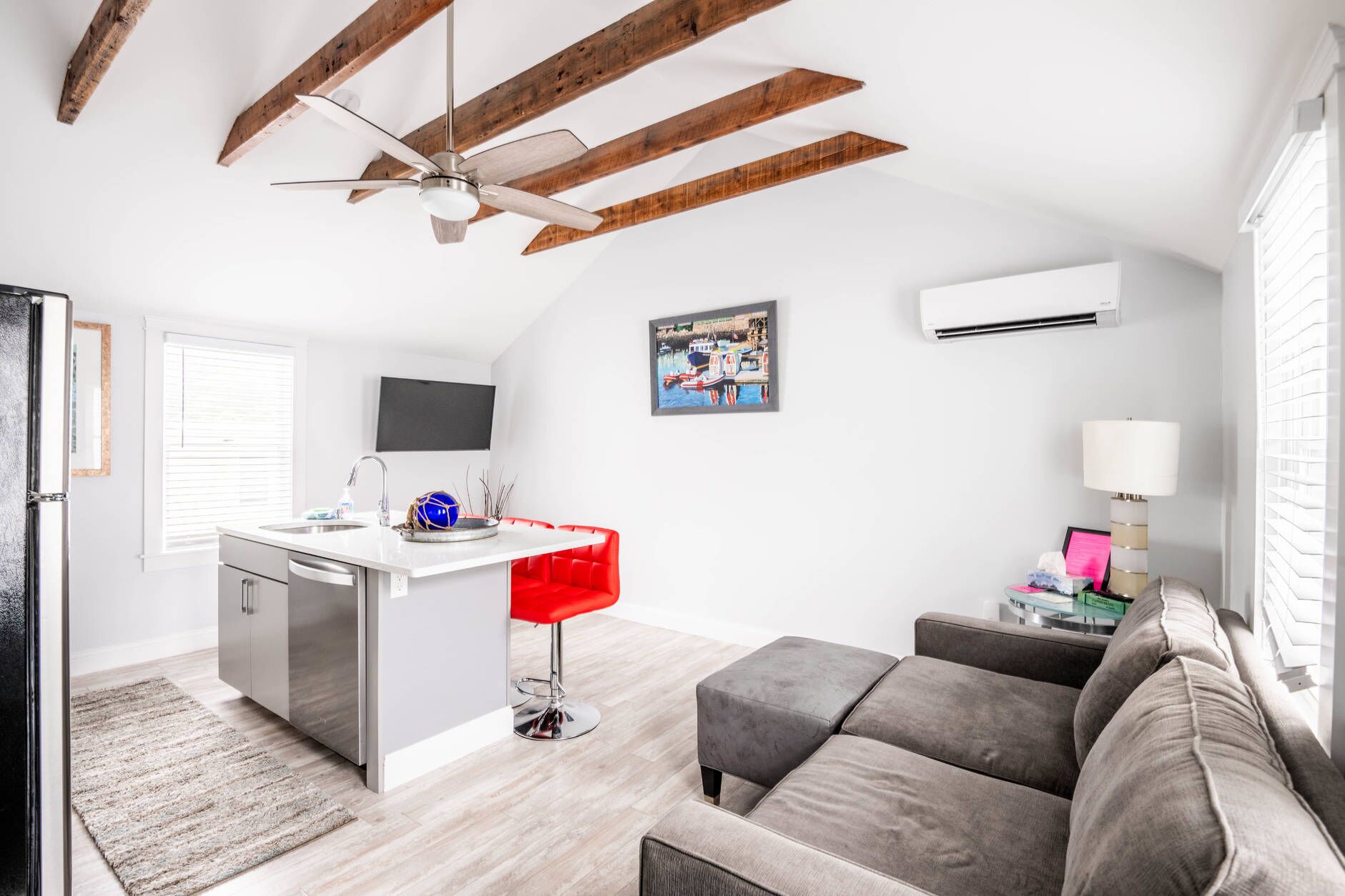 A modern kitchen with a central island, a red bar stool, a grey sofa, and a ceiling fan.