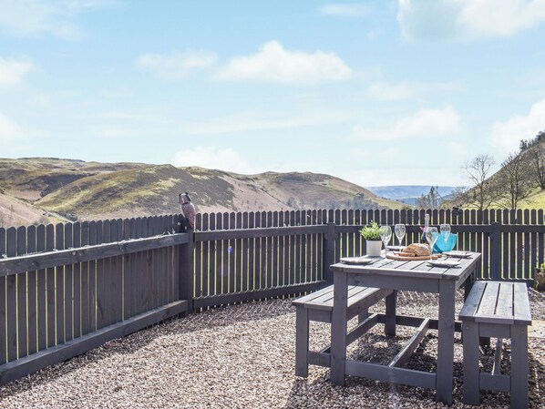 A wooden deck with a table and benches, overlooking a hilly landscape.