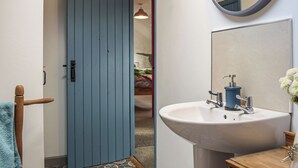Un baño con puerta azul, lavamanos blanco, espejo y toallero.