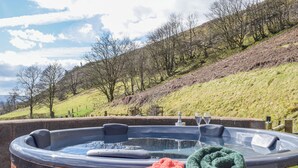 Un jacuzzi con revestimiento de madera, rodeado por una colina cubierta de hierba y árboles.