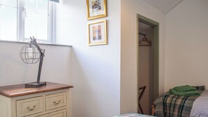 Un dormitorio con un aparador de madera, una cama con manta escocesa y una ventana con lámpara tipo globo.
