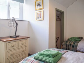 A bedroom with a wooden dresser, a bed with a plaid blanket, and a window with a globe lamp.