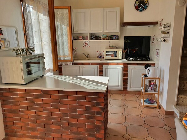 Una cocina compacta con encimera de ladrillo, armarios blancos, microondas y fregadero.