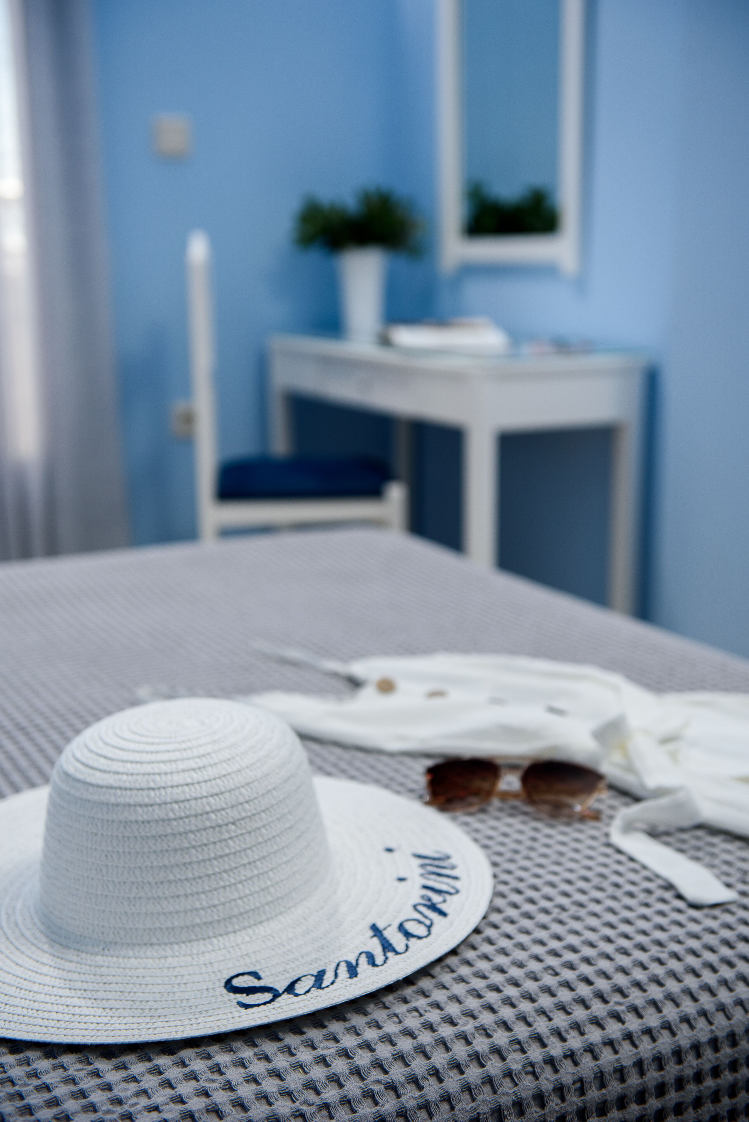 A white hat with "Santorini" embroidered on it, a white cloth, and a pair of sunglasses on a textured grey surface.